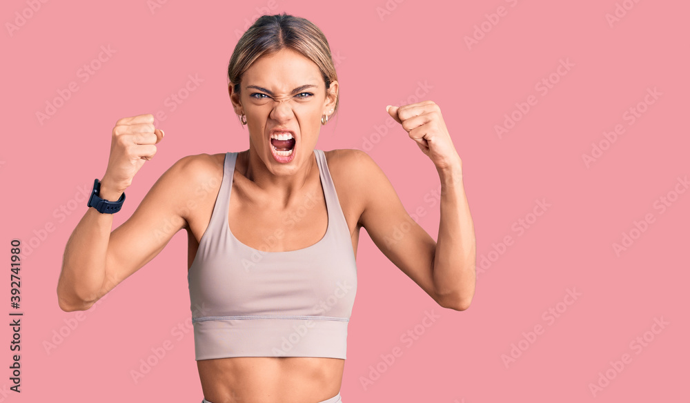 Beautiful caucasian woman wearing sportswear angry and mad raising fists frustrated and furious while shouting with anger. rage and aggressive concept. Beautiful caucasian woman wearing sportswear angry and mad raising fists frustrated and furious while shouting with anger. rage and aggressive concept.