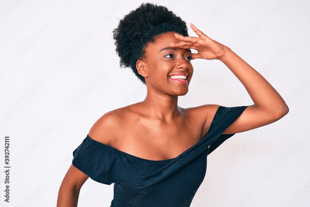 Young african american woman wearing casual clothes very happy and smiling looking far away with hand over head. searching concept. Young african american woman wearing casual clothes very happy and smiling looking far away with hand over head. searching concept.