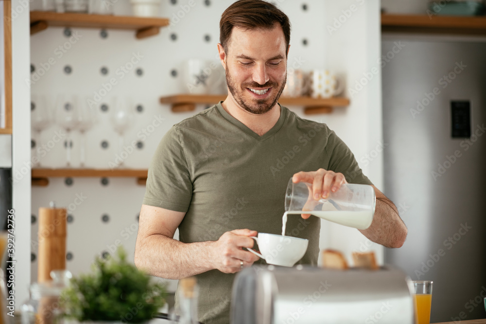 Handsome man preparing breakfast at home. Young man drinking coffee while preparing sandwich. Handsome man preparing breakfast at home. Young man drinking coffee while preparing sandwich.