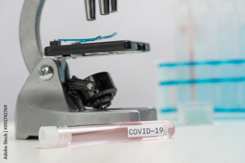 Close-up view of biological tube with covid-19 vaccine on microscope background. Examines of coronavirus in laboratory. Healthcare and medical concept.