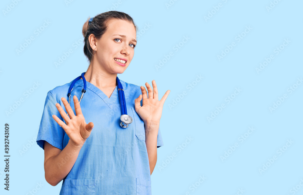 Young beautiful blonde woman wearing doctor uniform and stethoscope disgusted expression, displeased and fearful doing disgust face because aversion reaction. with hands raised Young beautiful blonde woman wearing doctor uniform and stethoscope disgusted expression, displeased and fearful doing disgust face because aversion reaction. with hands raised