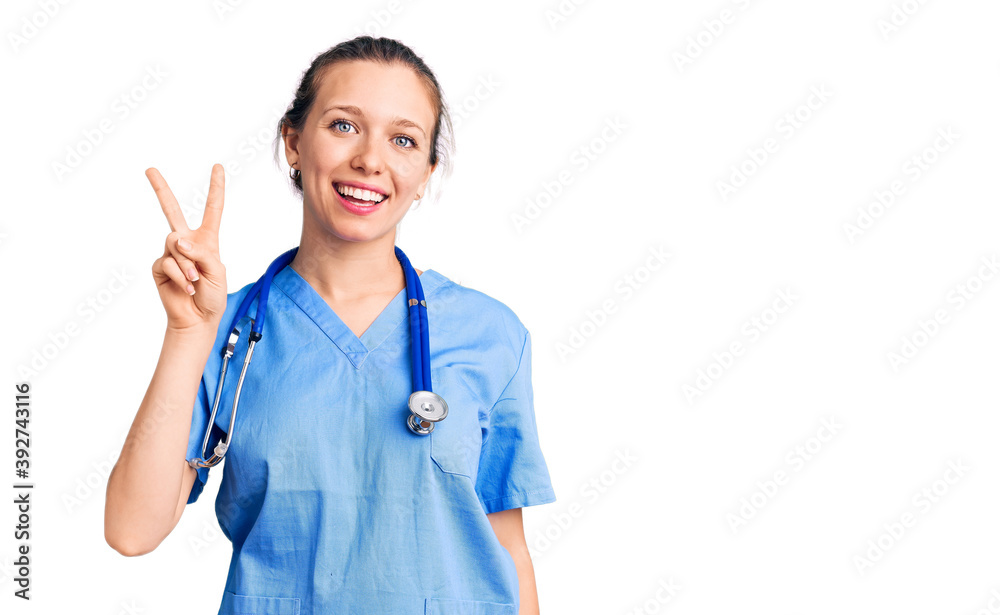 Young beautiful blonde woman wearing doctor uniform and stethoscope showing and pointing up with fingers number two while smiling confident and happy. Young beautiful blonde woman wearing doctor uniform and stethoscope showing and pointing up with fingers number two while smiling confident and happy.