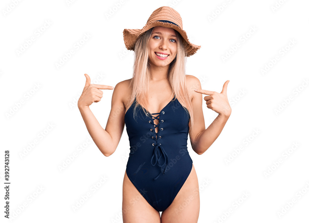 Young beautiful blonde woman wearing swimwear and summer hat looking confident with smile on face, pointing oneself with fingers proud and happy. Young beautiful blonde woman wearing swimwear and summer hat looking confident with smile on face, pointing oneself with fingers proud and happy.