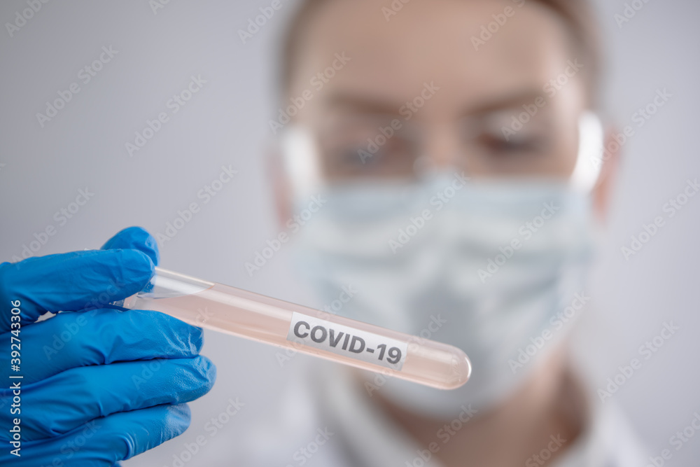 Close-up view of female microbiologist in biohazard protective clothing looking for biological tube with covid-19 sample. Research and development concept. Close-up view of female microbiologist in biohazard protective clothing looking for biological tube with covid-19 sample. Research and development concept.