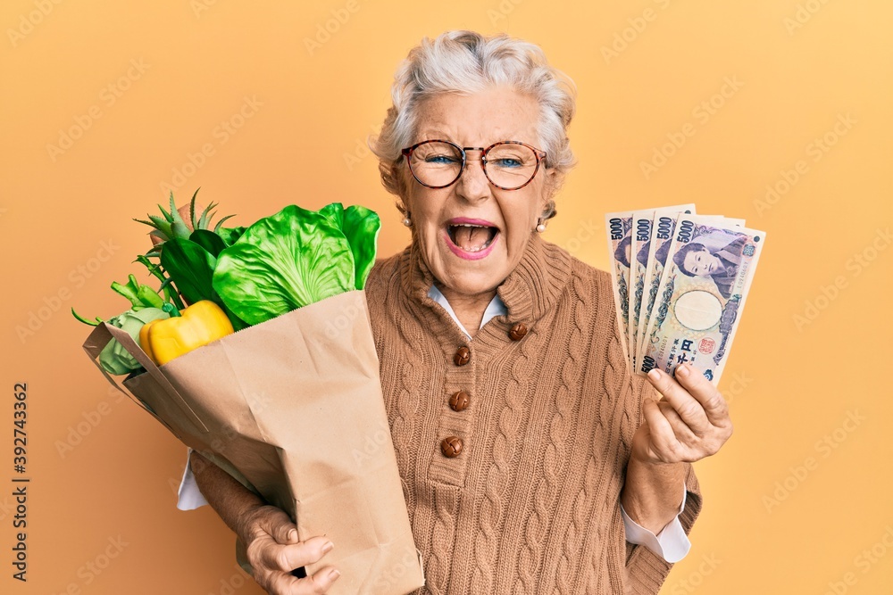 Senior grey-haired woman holding groceries and japanes yen banknotes smiling and laughing hard out loud because funny crazy joke. Senior grey-haired woman holding groceries and japanes yen banknotes smiling and laughing hard out loud because funny crazy joke.