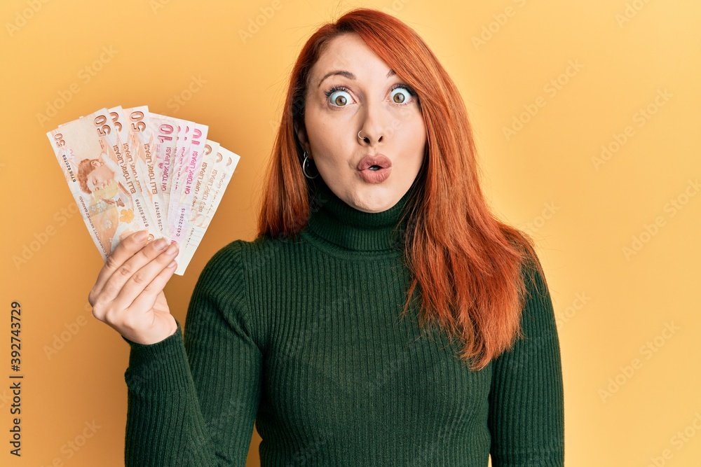 Beautiful redhead woman holding turkish lira banknotes scared and amazed with open mouth for surprise, disbelief face Beautiful redhead woman holding turkish lira banknotes scared and amazed with open mouth for surprise, disbelief face