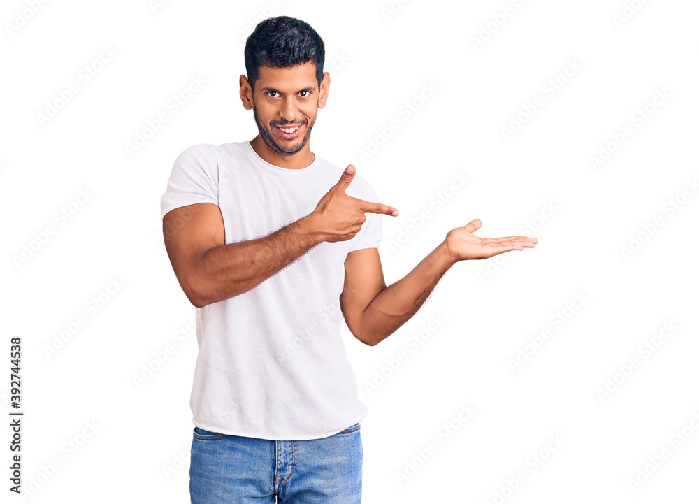 Young latin man wearing casual clothes amazed and smiling to the camera while presenting with hand and pointing with finger. Young latin man wearing casual clothes amazed and smiling to the camera while presenting with hand and pointing with finger.