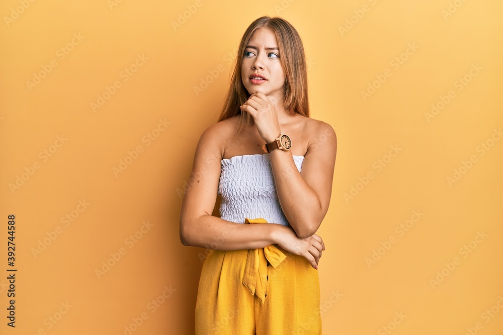 Beautiful young blonde woman wearing casual summer clothes with hand on chin thinking about question, pensive expression. smiling with thoughtful face. doubt concept. Beautiful young blonde woman wearing casual summer clothes with hand on chin thinking about question, pensive expression. smiling with thoughtful face. doubt concept.