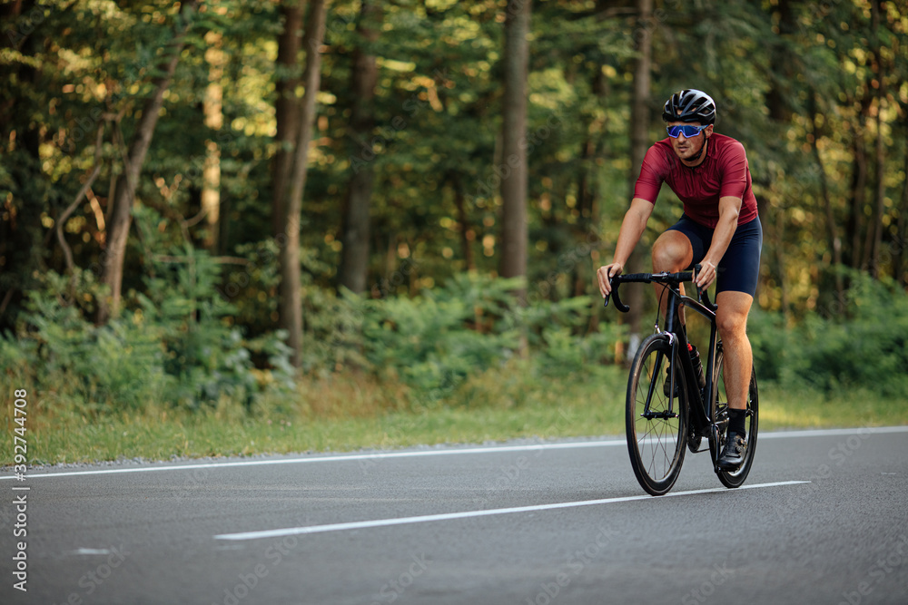 Muscular guy in helmet riding bike on asphalt road