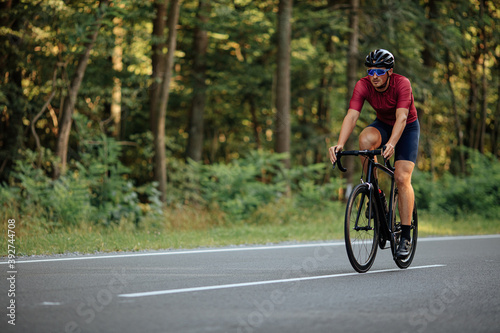 Muscular guy in helmet riding bike on asphalt road