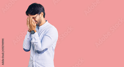 Handsome hispanic man wearing business shirt and glasses with sad expression covering face with hands while crying. depression concept. photo