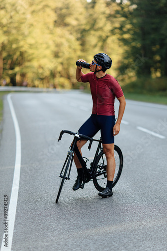 Strong man drinking water while standing on road with bike