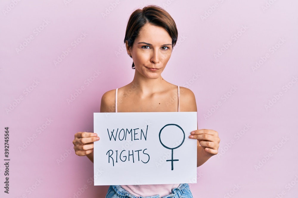 Young brunette woman with short hair holding woman rights banner skeptic and nervous, frowning upset because of problem. negative person. Young brunette woman with short hair holding woman rights banner skeptic and nervous, frowning upset because of problem. negative person.
