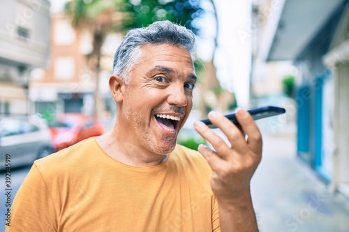 Middle age grey-haired man smiling happy talking on the smartphone at street of city.