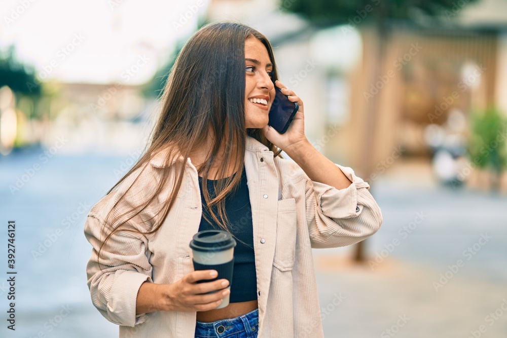 Young hispanic girl smiling happy talking on the smartphone and drinking take away coffee at the city.
