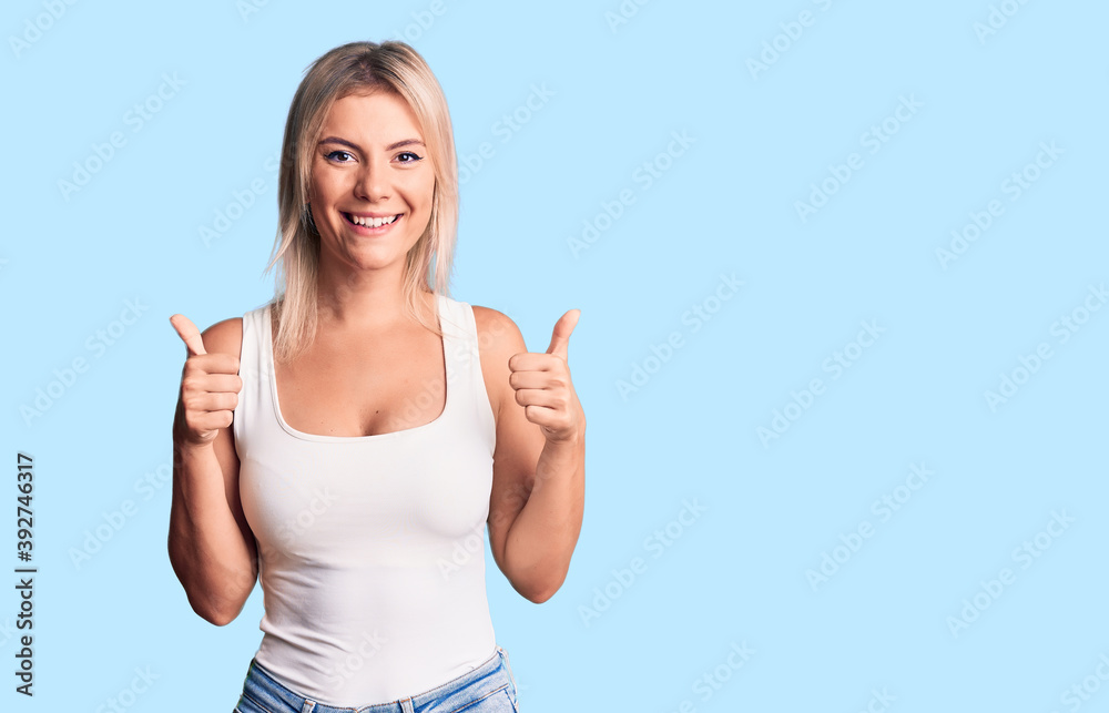 Young beautiful blonde woman wearing casual sleeveless t-shirt success sign doing positive gesture with hand, thumbs up smiling and happy. cheerful expression and winner gesture.