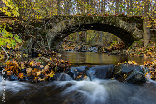 A Water cascade in the creek flowing under an ancient stone bridge in the autumn forest.