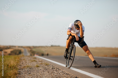 Fototapeta Naklejka Na Ścianę i Meble -  Exhausted cyclist relaxing on road after long riding