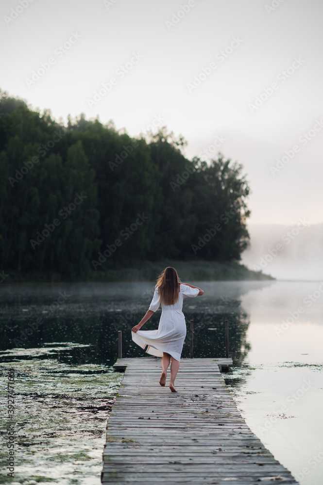 Woman in white light dress run on the pier on foggy morning lake. Woman in white light dress run on the pier on foggy morning lake.