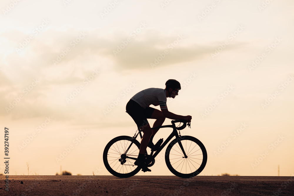 Fototapeta premium Silhouette of man in helmet riding bike during sunset
