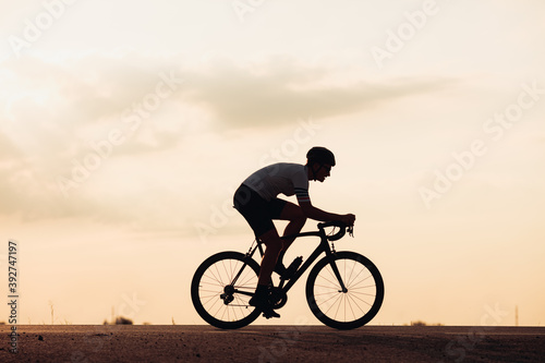 Silhouette of man in helmet riding bike during sunset