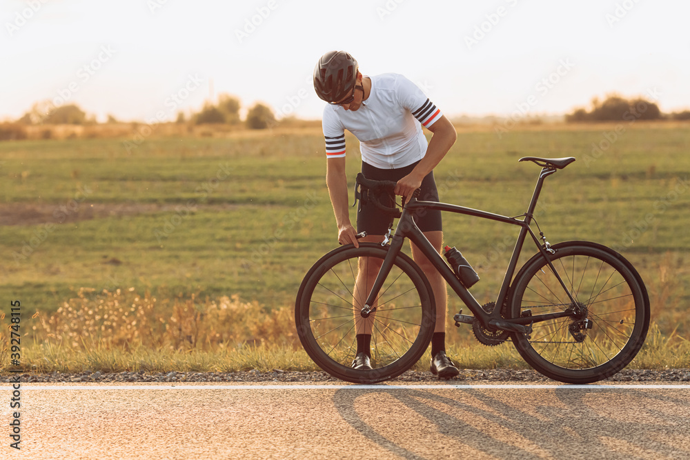Fototapeta premium Muscular cyclist checking wheel on bike outdoors