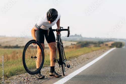 Strong cyclist in sportswear repairing wheel on bike