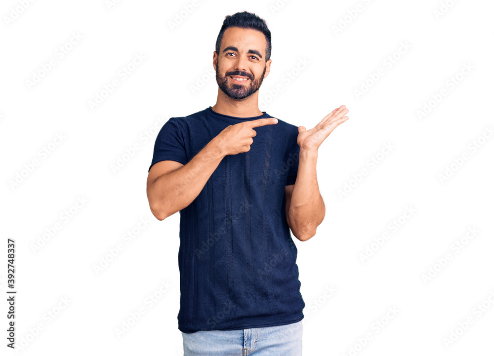 Young hispanic man wearing casual clothes amazed and smiling to the camera while presenting with hand and pointing with finger. Young hispanic man wearing casual clothes amazed and smiling to the camera while presenting with hand and pointing with finger.