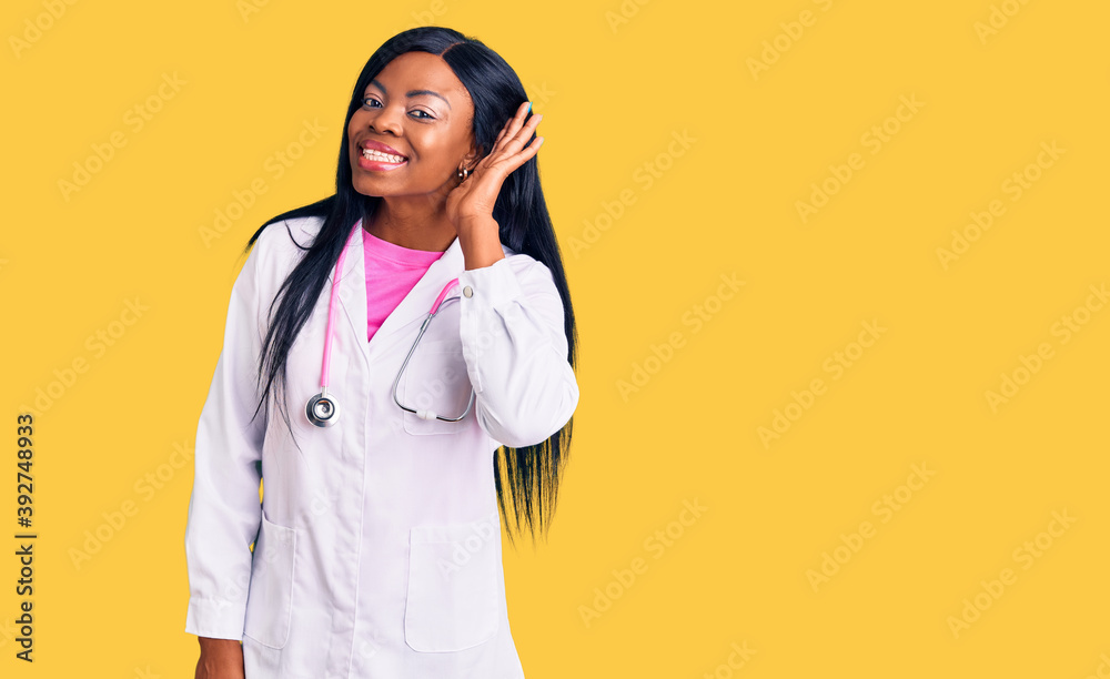 Young african american woman wearing doctor stethoscope smiling with hand over ear listening an hearing to rumor or gossip. deafness concept.