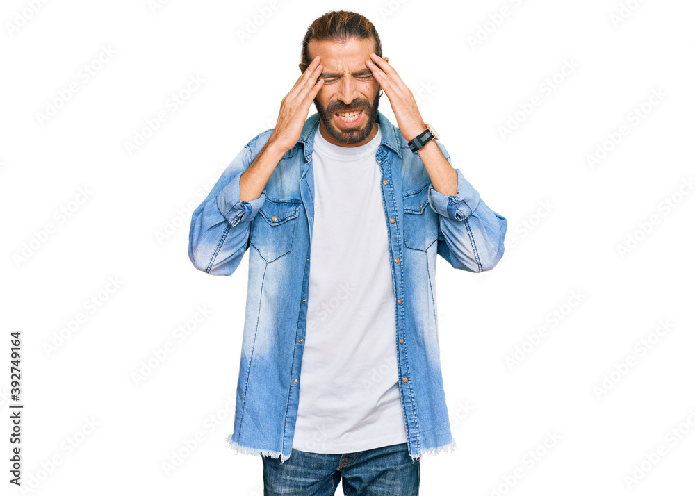 Attractive man with long hair and beard wearing casual denim jacket with hand on head, headache because stress. suffering migraine. Attractive man with long hair and beard wearing casual denim jacket with hand on head, headache because stress. suffering migraine.