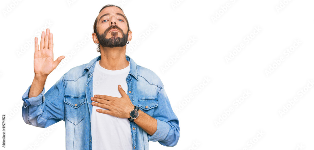 Fototapeta premium Attractive man with long hair and beard wearing casual denim jacket swearing with hand on chest and open palm, making a loyalty promise oath