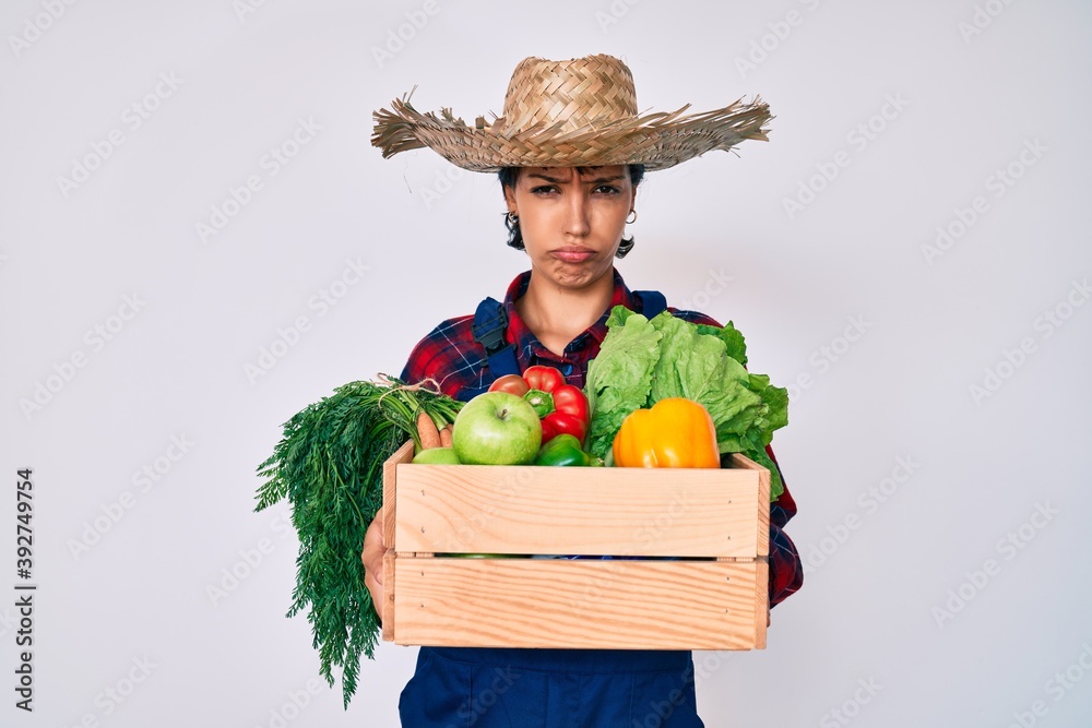 Beautiful brunettte woman wearing farmer clothes holding vegetables depressed and worry for distress, crying angry and afraid. sad expression.