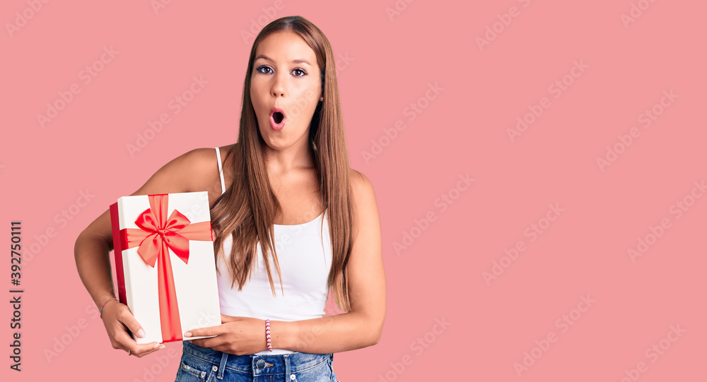 Young beautiful hispanic woman holding gift scared and amazed with open mouth for surprise, disbelief face Young beautiful hispanic woman holding gift scared and amazed with open mouth for surprise, disbelief face