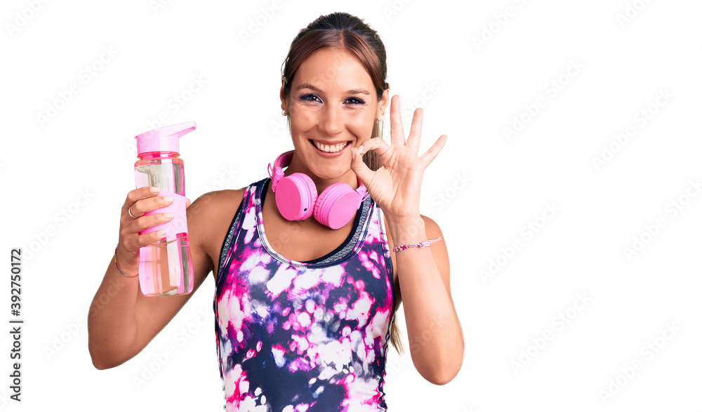 Young beautiful hispanic woman wearing sportswear holding water bottle doing ok sign with fingers, smiling friendly gesturing excellent symbol Young beautiful hispanic woman wearing sportswear holding water bottle doing ok sign with fingers, smiling friendly gesturing excellent symbol