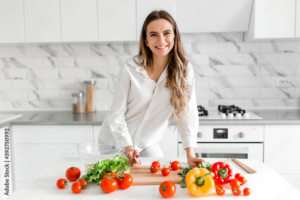 Happy young pretty woman preparing salad in kitchen. Cooking homemade food.