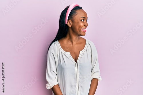 Young african woman wearing casual clothes over pink background looking away to side with smile on face, natural expression. laughing confident.