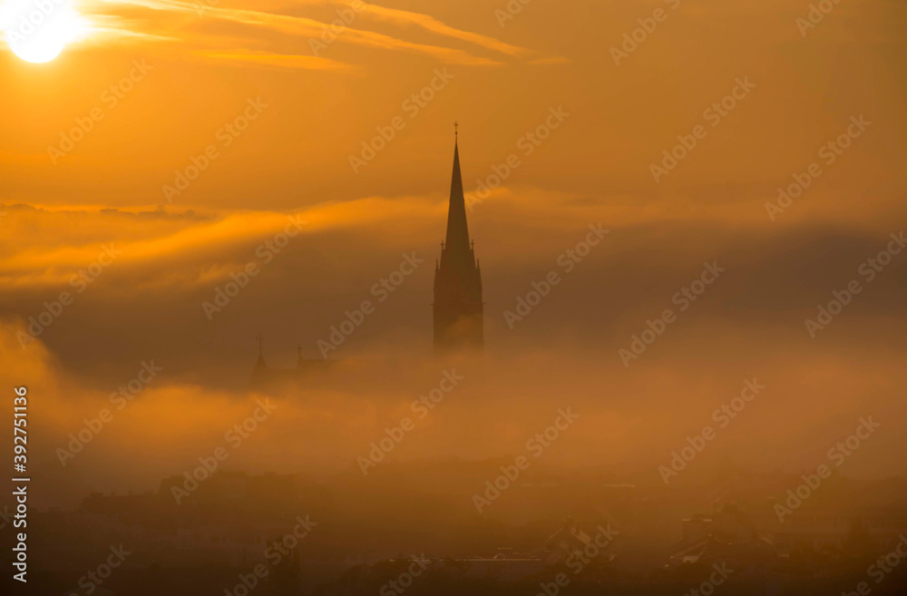 Fototapeta premium Cityscape of Graz with Church of the Sacred Heart of Jesus and historic buildings, in Graz, Styria region, Austria, at sunrise. Beautiful foggy morning over the city of Graz, in autumn