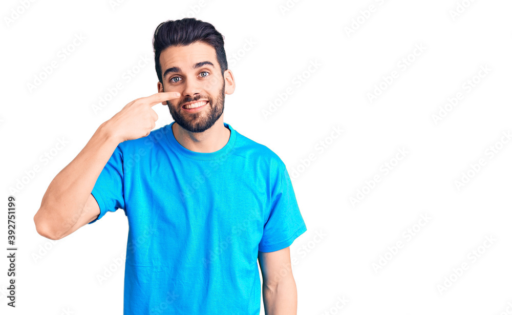 Young handsome man with beard wearing casual t-shirt pointing with hand finger to face and nose, smiling cheerful. beauty concept Young handsome man with beard wearing casual t-shirt pointing with hand finger to face and nose, smiling cheerful. beauty concept