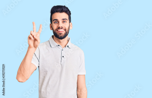 Young handsome man with beard wearing casual polo showing and pointing up with fingers number two while smiling confident and happy.