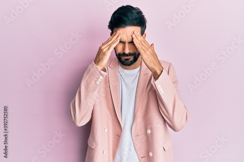 Young hispanic man with beard wearing pink elegant jacket very happy and smiling looking far away with hand over head. searching concept.