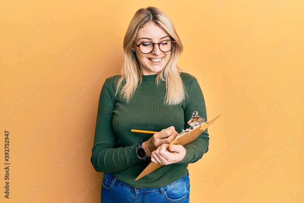 Young caucasian woman writing on checklist clipboard smiling with a happy and cool smile on face. showing teeth. Young caucasian woman writing on checklist clipboard smiling with a happy and cool smile on face. showing teeth.