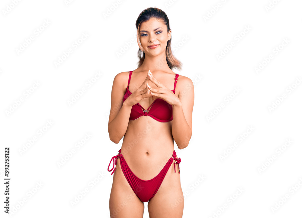 Naklejka premium Young beautiful woman wearing bikini hands together and fingers crossed smiling relaxed and cheerful. success and optimistic