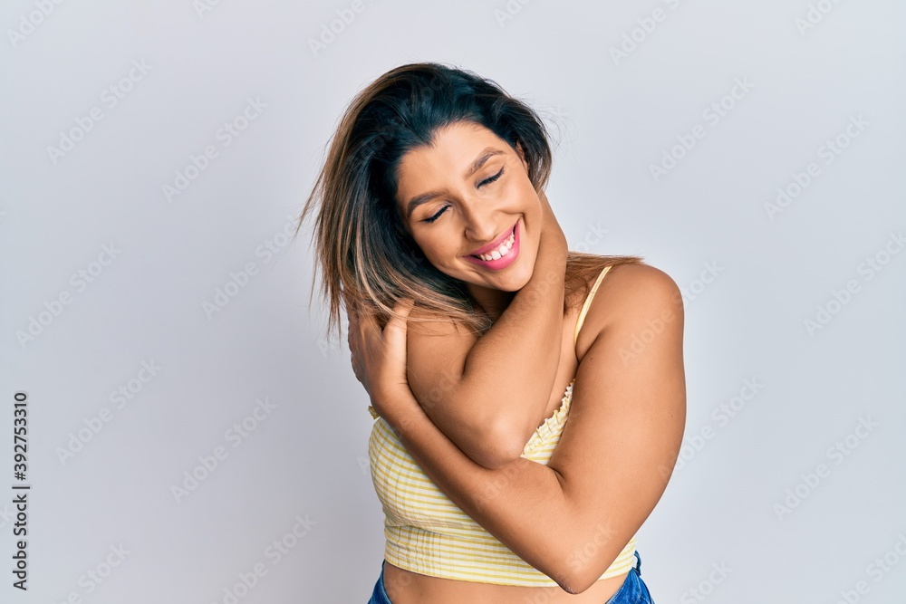 Fototapeta premium Beautiful brunette woman wearing casual clothes hugging oneself happy and positive, smiling confident. self love and self care