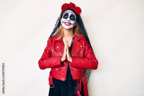 Woman wearing day of the dead costume over white begging and praying with hands together with hope expression on face very emotional and worried. begging.
