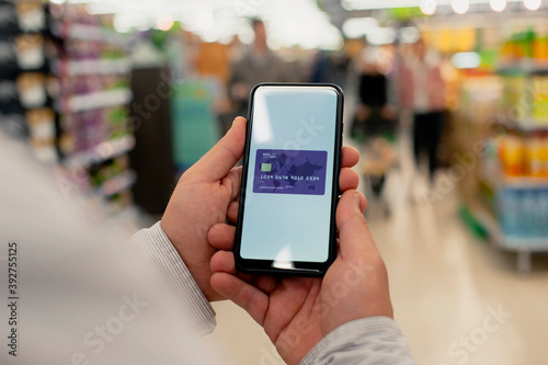 A man holds a smartphone with a credit card in his hands on the background of a grocery store.