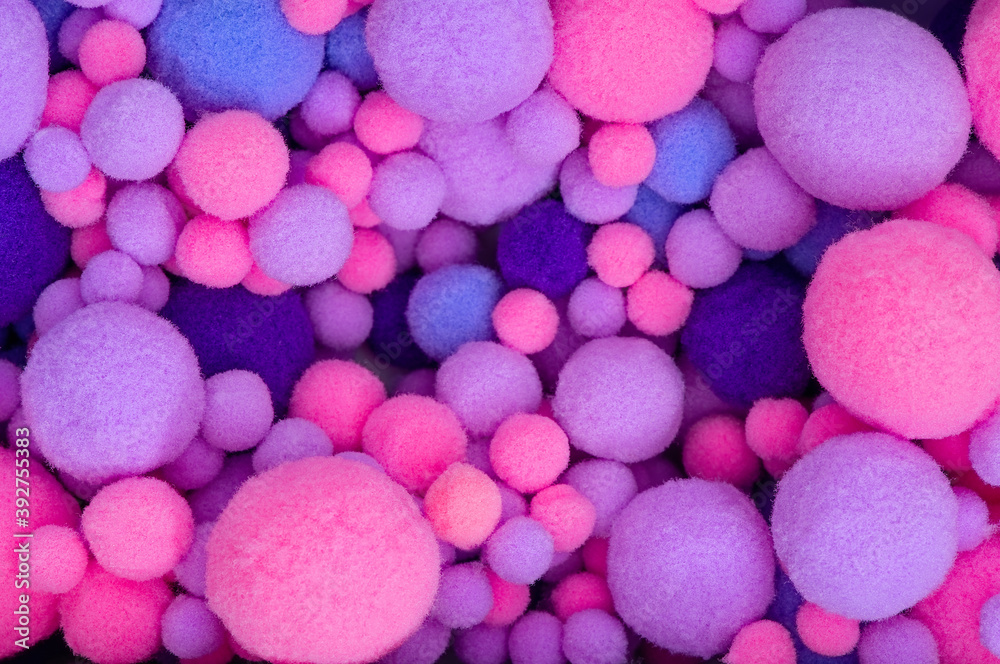 Background from multi-colored pom-poms of different sizes. Pink, violet and violet furry pom-pons in a heap close-up. Background from multi-colored pom-poms of different sizes. Pink, violet and violet furry pom-pons in a heap close-up.