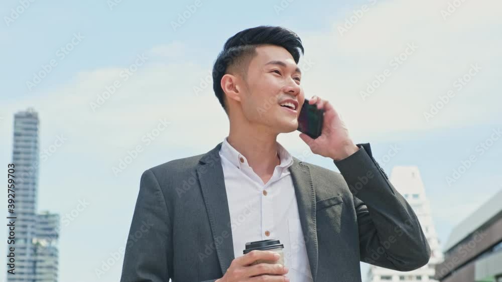 Asian young businessman talking on mobile phone, walking to the office Asian young businessman talking on mobile phone, walking to the office