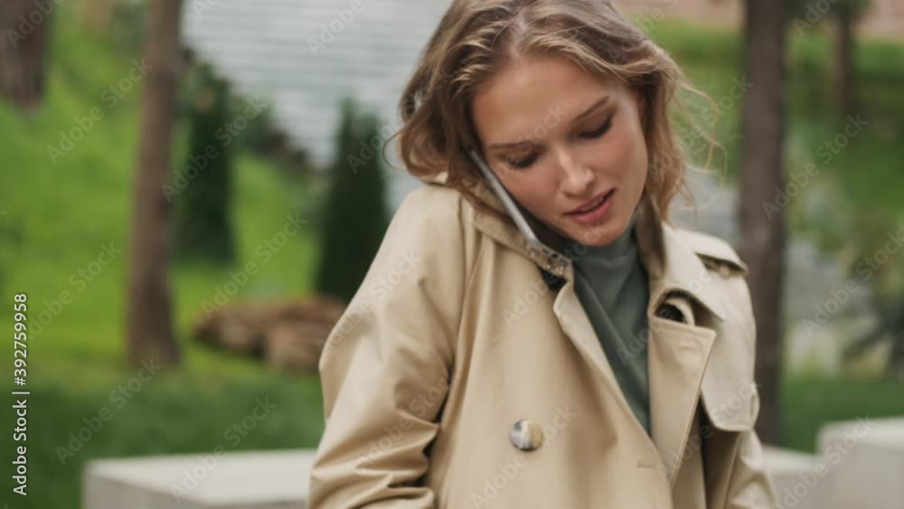 Tracking out shot of stylish blond student girl talking on phone making notes in notepad studying on bench in park Tracking out shot of stylish blond student girl talking on phone making notes in notepad studying on bench in park