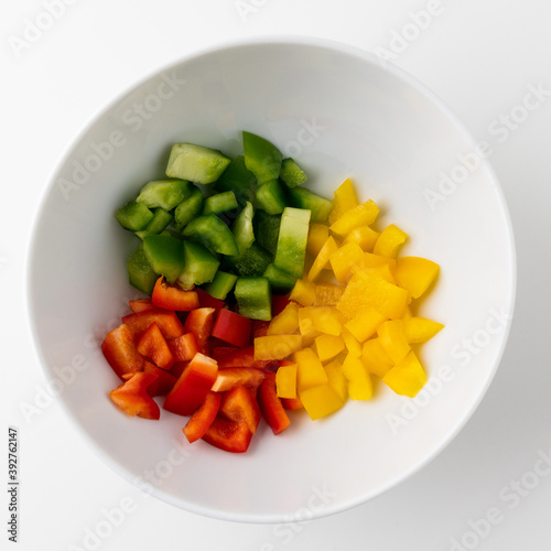 Raw mixed red yellow and green bell pepper cut into small pieces put on a bowl. Healthy vegetables and food on isolated white background.