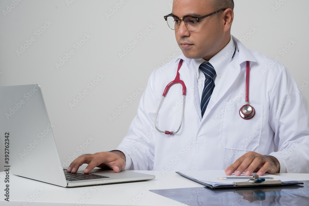 A portrait of Asian doctor put on stethoscope working on laptop sitting at the desk isolated on white background. A portrait of Asian doctor put on stethoscope working on laptop sitting at the desk isolated on white background.